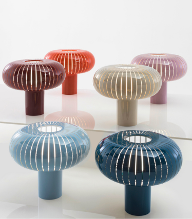 Six lampes à poser décoratives de la marque Kartell, proposées dans différentes couleurs, présentent un design cannelé en forme de champignon et sont disposées sur une surface réfléchissante.