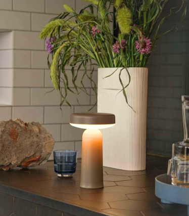 Lampe de table portable Muuto sur un plan de travail de cuisine sombre avec décoration florale.