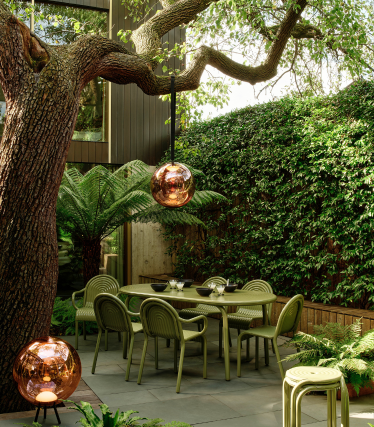Lampes d’extérieur Tom Dixon dans un jardin élégant avec coin repas sous un vieil arbre.