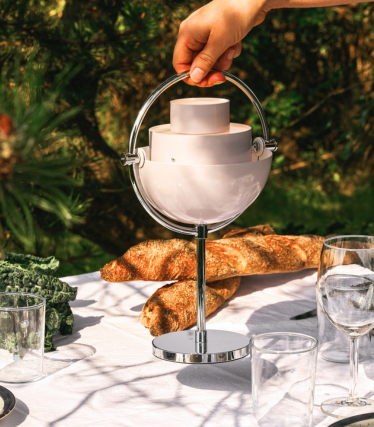 Lampe de table portable GUBI sur une table de jardin élégamment dressée au soleil.