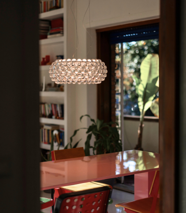 Suspension sphérique composée de globes en verre au-dessus d’une table à manger rouge, vue à travers une porte.